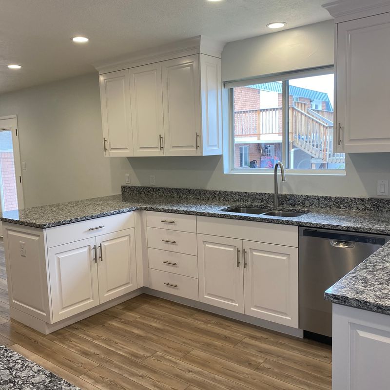 A modern kitchen featuring white cabinets, white and grey granite countertops and stainless steel features.